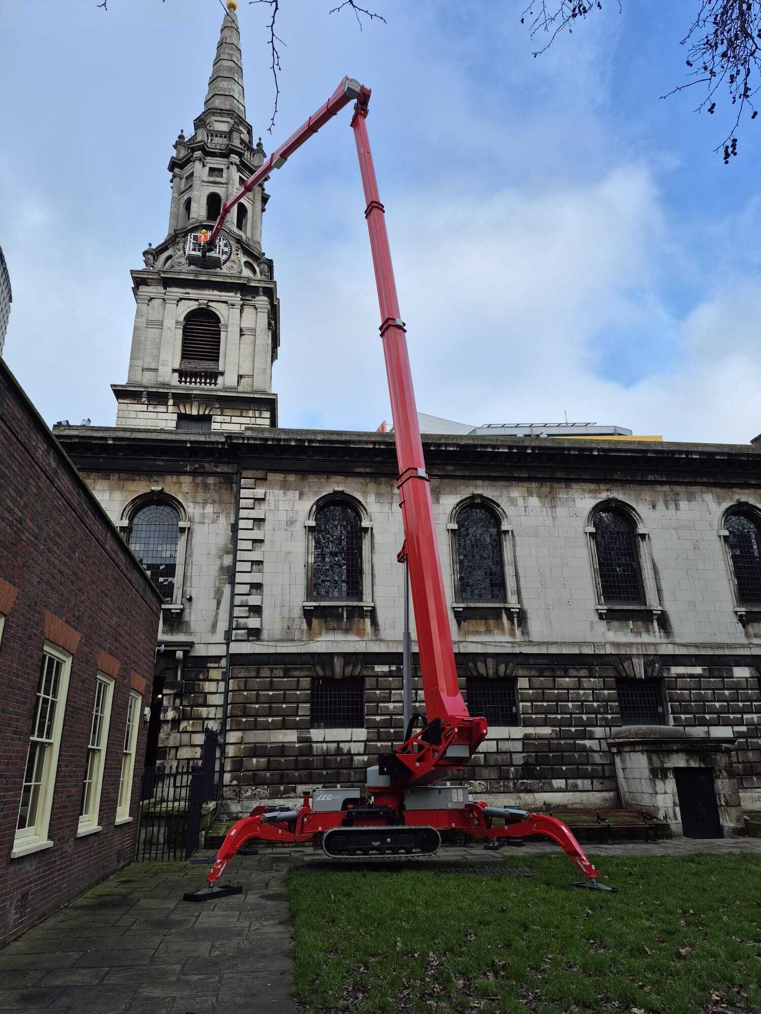 Red spider lift set on outriggers beside a church with an operator raised to the tower